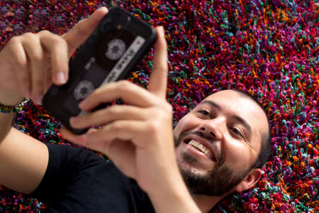 latino man lying on carpet texting on cell phone. Smiling man. Concept of technology.