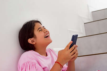 Girl sitting on the stairs, laughing loudly with phone in her hands. Smiling girl. Concept of...