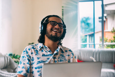 young latino man smiling in front of his computer with headphones. Virtual meeting. New Normal