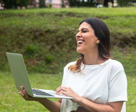 latina woman standing with laptop in park. Fresh airの写真素材