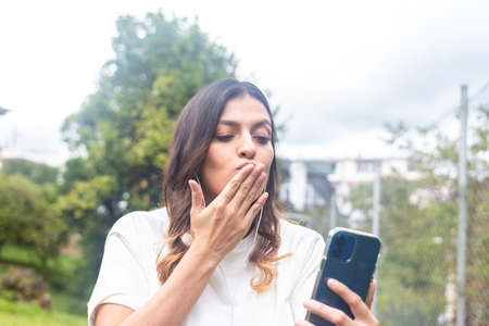 latina woman blowing a kiss to cell phone camera in video call. Fresh airの写真素材