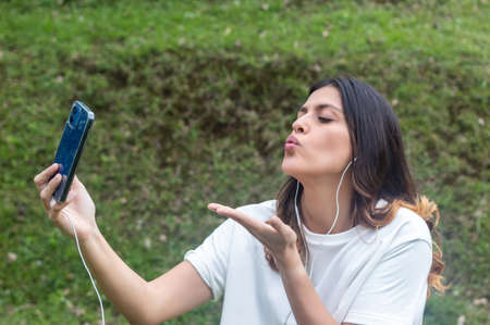 Young woman blowing kiss while taking selfie at the park. Fresh airの写真素材