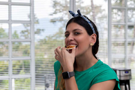 latina woman with scarf in kitchen eating a snackの写真素材