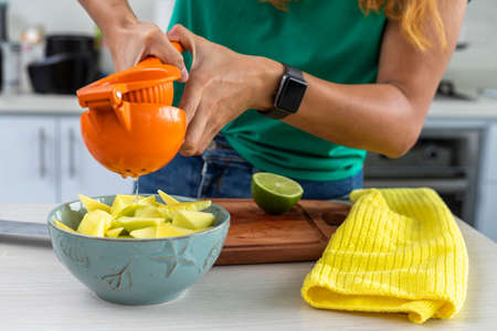 woman squeezing lemon over mango in a bowl in the kitchenの写真素材