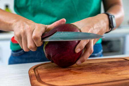 woman cutting a mango in the kitchen on a wooden boardの写真素材