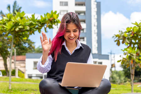 young woman sitting outdoors waving at the screen of her laptopの写真素材