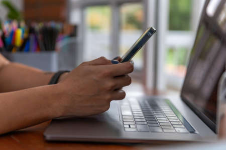 Close Up Of Person At Laptop Using Mobile Phoneの写真素材