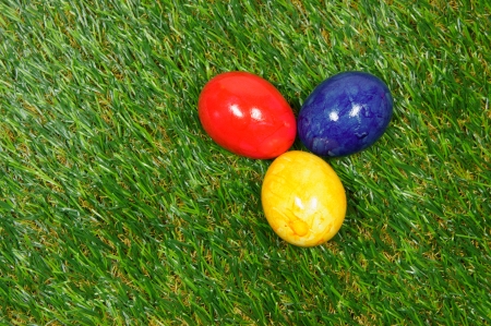 three colorful eggs lie on a synthetic grassの写真素材
