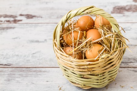 Natural brown eggs in a straw basket on white wooden backgroundの写真素材