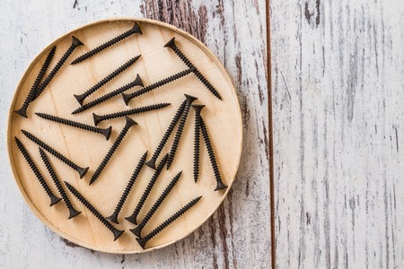 Group of used, old and black screws on wooden bowl