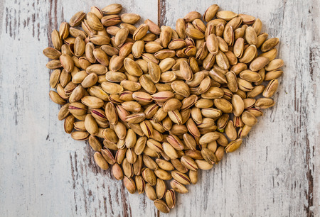 Heart shaped pistachio nuts on white wooden backgroundの写真素材