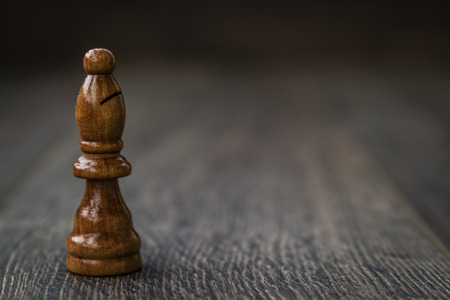 Black Bishop, chess piece on a brown wooden table and backgroundの写真素材