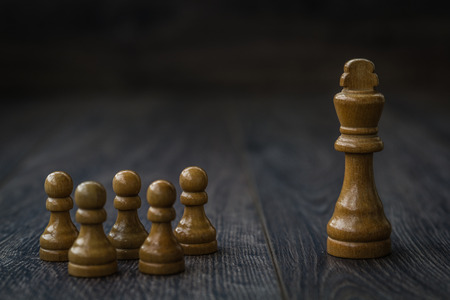 White pawns against king on a brown wooden table and backgroundの写真素材