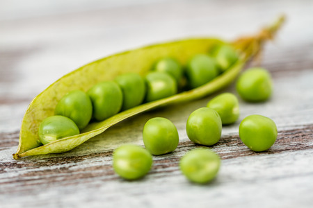 Fresh raw green peas on white wooden background