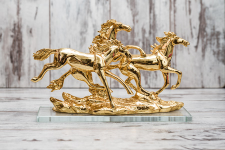 Statuettes of golden horses on white wooden backgroundの写真素材