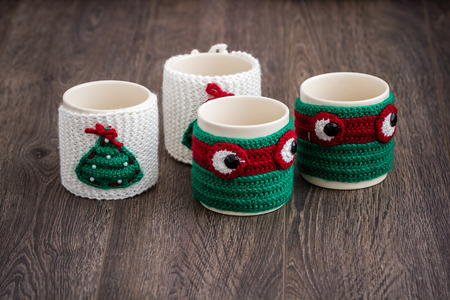Mugs in knitted mittens, decorated for Christmas, on brown wooden backgroundの写真素材