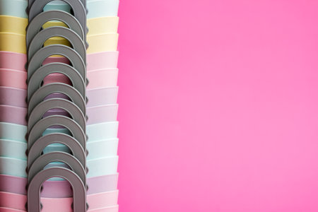 Stack of colorful plastic cups arranged in a gradient of pastel rainbow colors against a pink...
