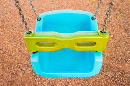 Close view of a blue plastic baby swing with green safety bar on a playground.の写真素材