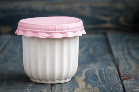 White ceramic jar with pastel pink colored silicone lid on a blue rustic wooden surface with copy space.の写真素材