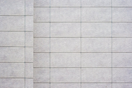 Close up of a tiled wall with a grid pattern, featuring light gray tiles and dark grout lines, as texture, background.の写真素材