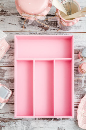 Pink cutlery tray with compartments on a rustic wooden surface surrounded by kitchen items like jars and utensils offering a charming kitchen organization solution.の写真素材