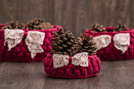 Handmade knitted baskets adorned with lace bows and filled with pine cones offering a rustic and cozy decorative touch for home interiors.の写真素材
