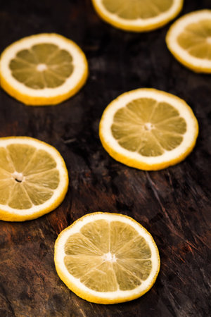 Sliced lemons arranged on a dark surface showcasing their fresh and vibrant yellow color with a rustic touch.の写真素材