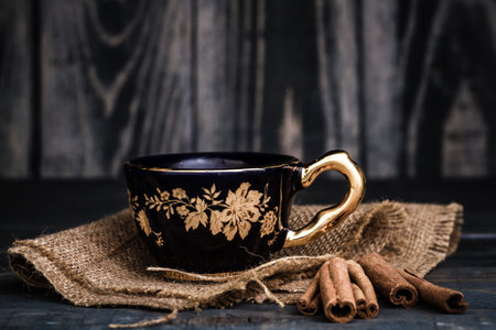 Elegant black and gold teacups with floral designs on a dark wooden surface.の写真素材