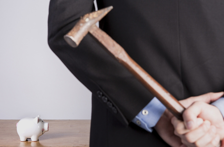 Businessman hiding a hammer in his hand and stands in front of a piggy bankの写真素材