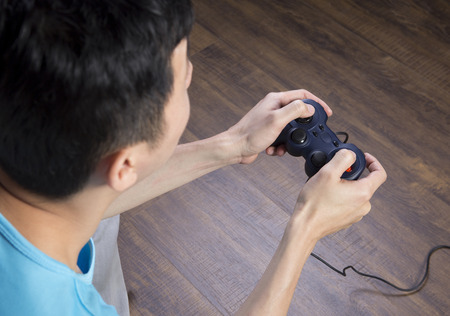 asian man sitting on the floor, playing games with black joystick, back viewの写真素材
