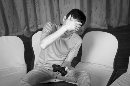 asian man sitting on the floor, playing games with joystick and looks sad, black and white photoの写真素材
