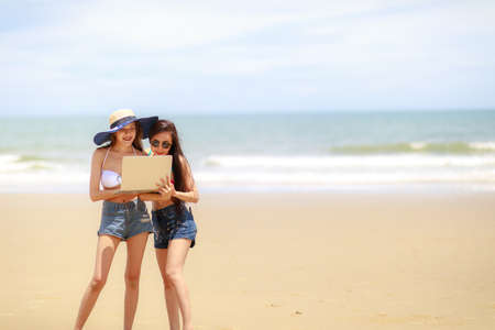 Two sexy woman with the notebook pc relaxing on the beachの写真素材