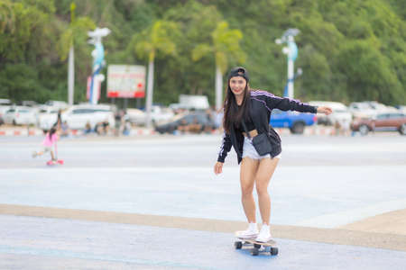 Asian woman playing surf skate or skates board outdoors on beautiful summer day. Happy young women play surf skate at park on morning time in the park.の写真素材