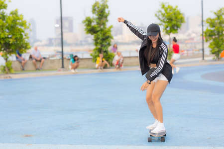 Asian woman playing surf skate or skates board outdoors on beautiful summer day. Happy young women play surf skate at park on morning time in the park.の写真素材