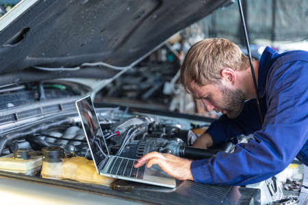 A Russian Male mechanic  with tablet pc computer making system diagnostic in car at workshop. car service, repair, technology, maintenance and people conceptの写真素材
