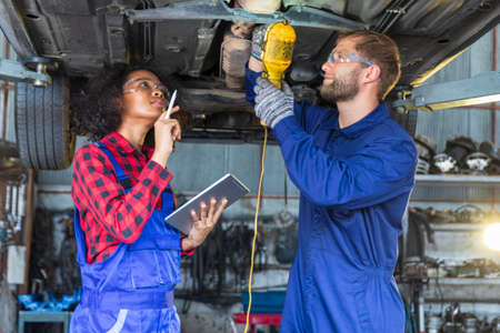Two mechanic male and female working togther upder car lift with digital tablet for car inspection.の写真素材