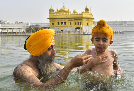 AMRITSAR, INDIA - APRIL 13:  A Sikh devotee with his child take a dip in the holy Sarovar (sacred water tank) on the occasion of Baisakhi festival at the Golden Temple on April 13, 2024 in Amritsar, India. Baisakhi or Vaisakhi, a popular spring festival tのeditorial素材