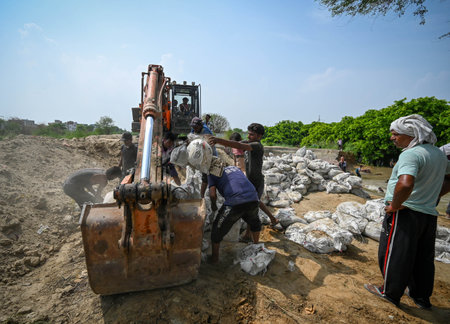 NEW DELHI, INDIA - JULY 11: Workers from the flood control department seen filling sand bags at the spot from where the Munak canal breaches at JJ Colony, Bawana on July 11, 2024 in New Delhi, India. A breach in the canal, that supplies water from Haryanaのeditorial素材