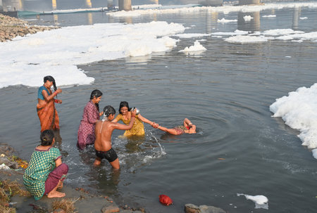NEW DELHI, INDIA - NOVEMBER 3: Devotees perform pre-Chhath Puja rituals as toxic foam floats on the surface of the Yamuna River at Kalindi Kunj on November 3, 2024 in New Delhi, India. The Yamuna River is inundated with toxic foam ahead of Chhath Puja, seのeditorial素材