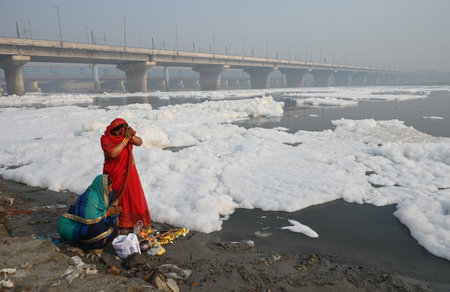 NEW DELHI, INDIA - NOVEMBER 3: Devotees perform pre-Chhath Puja rituals as toxic foam floats on the surface of the Yamuna River at Kalindi Kunj on November 3, 2024 in New Delhi, India. The Yamuna River is inundated with toxic foam ahead of Chhath Puja, seのeditorial素材