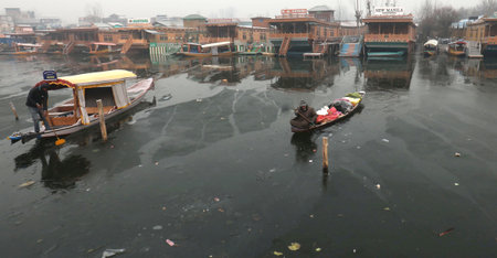 SRINAGAR INDIA DECEMBER 21 2024 A boatman makes his way through partially frozen surface parts of Dal Lake on December 21 2024 in Srinagar India Kashmir is in the grip of a cold wave and the 40 day period of Chillai Kalan major cold began in the Valley onのeditorial素材