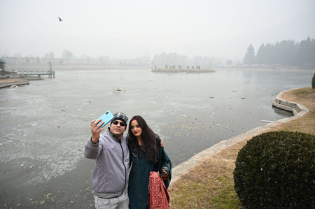 SRINAGAR INDIA DECEMBER 23 2024 Tourists take a selfie picture near a partially frozen pond on cold day on December 23 2024 in Srinagar India The freezing conditions have led to the freezing of water bodies disrupted water supply lines and increased dailyのeditorial素材
