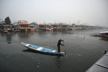 SRINAGAR, INDIA - DECEMBER 25: A boatman makes his way through frozen surface of Dal Lake on a cold morning, on December 25, 2024 in Srinagar, India. Kashmir is witnessing freezing night temperatures with Srinagar recorded minus 7.3 degrees Celsius. (Photのeditorial素材