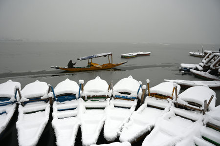 SRINAGAR, INDIA - DECEMBER 28: A boatman clears snow from his shikara boat at Dal Lake during the snowfall on December 28, 2024 in Srinagar, India. The Kashmir Valley received the season's heaviest snowfall on Saturday which threw normal life out of gear,のeditorial素材