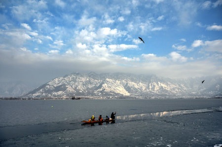 SRINAGAR, INDIA - DECEMBER 30: A man rows his boat through a frozen surface of Dal Lake against snow covered mountains in the backdrop on December 30, 2024 in Srinagar, India. Kashmir received heavy snowfall on Friday and Saturday, resulting in some areasのeditorial素材