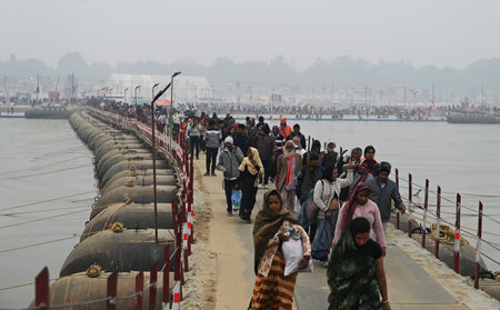 PRAYAGRAJ, INDIA - JANUARY 12: Devotees cross the pontoon bridge as they arrive to take dip into...
