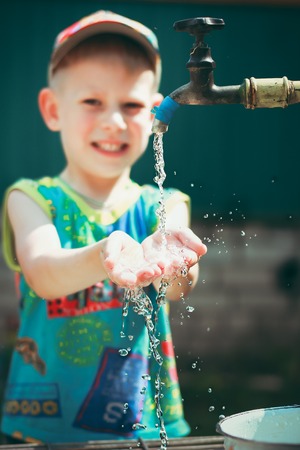 Young boy is washing a hand with summer waterの写真素材