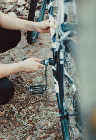 Repair of bike. Young man repairing a broken bicycle in the woods with wrenchの写真素材