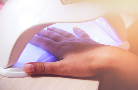 Woman hand inside lamp for nails on table close up. UV lamp for drying nails with gel method. violet nails dried in the lampの写真素材