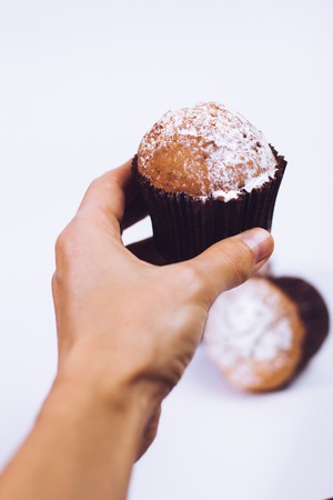 man hand holding a chocolate muffin whith sugar powder on white backgroundの写真素材